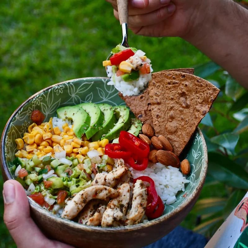 Chicken and avocado salad bowl with corn and tomatoes, similar to a taco-style salad, with a bread slice on the side