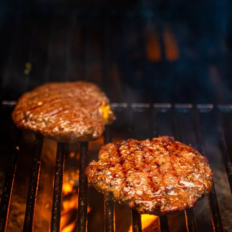 Beef burger patties cooking on a grill, the gluten free core of a Wendy's bunless burger