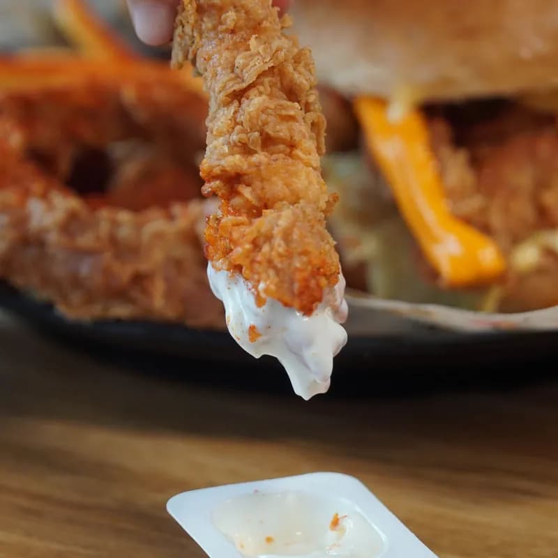 Crispy breaded chicken tender dipped in sauce, shown as a not gluten free chicken choice