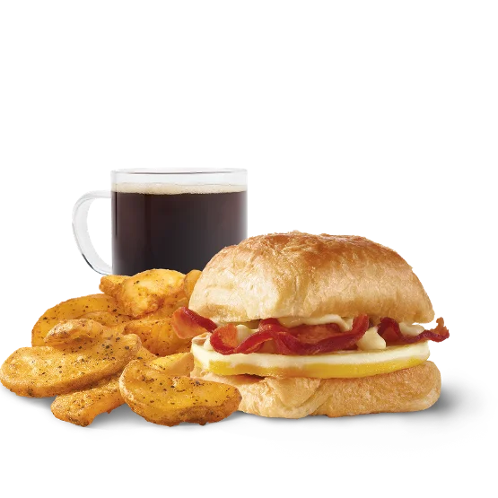 Close-up of Wendy’s Bacon, Egg & Swiss Croissant Combo with crispy bacon, fluffy egg, melted Swiss cheese, a flaky croissant, breakfast potatoes, and a drink.