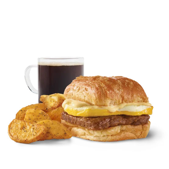 Close-up of Wendy’s Sausage, Egg & Swiss Croissant Combo with a flaky croissant sandwich, crispy breakfast potatoes, and a cold drink.