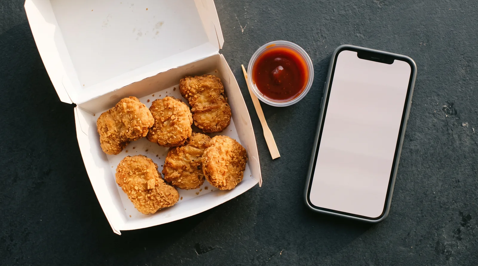 Wendy's free 6 piece chicken nuggets in a carton beside a smartphone for app ordering